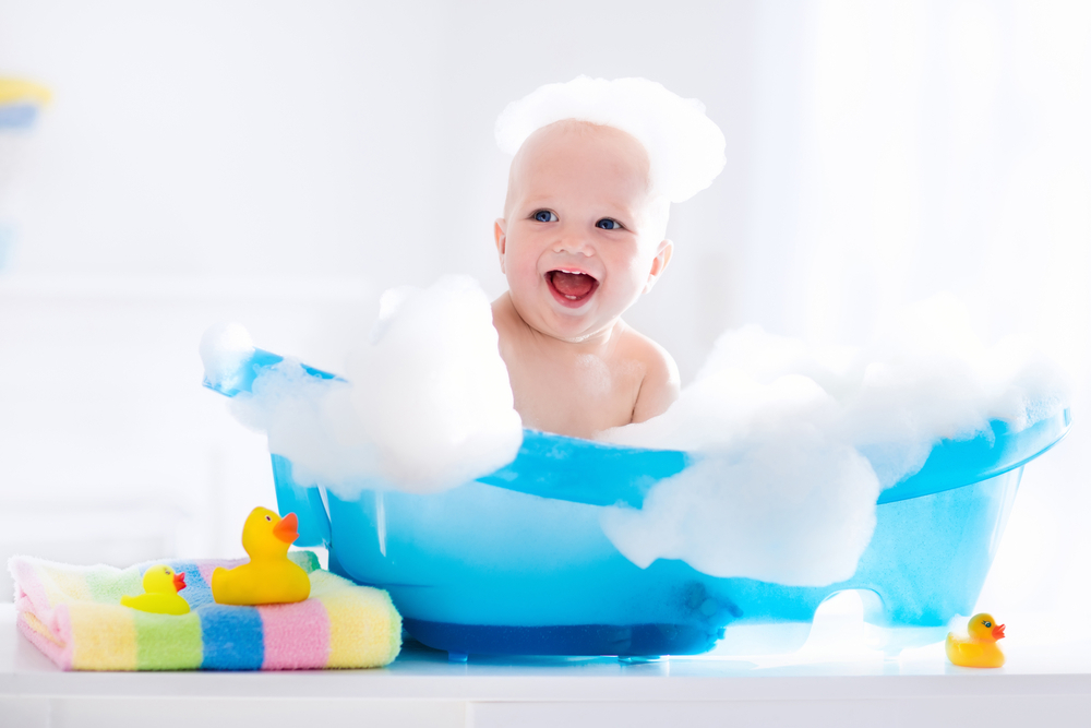 Glad leende baby tar et bad og leker med skumbobler